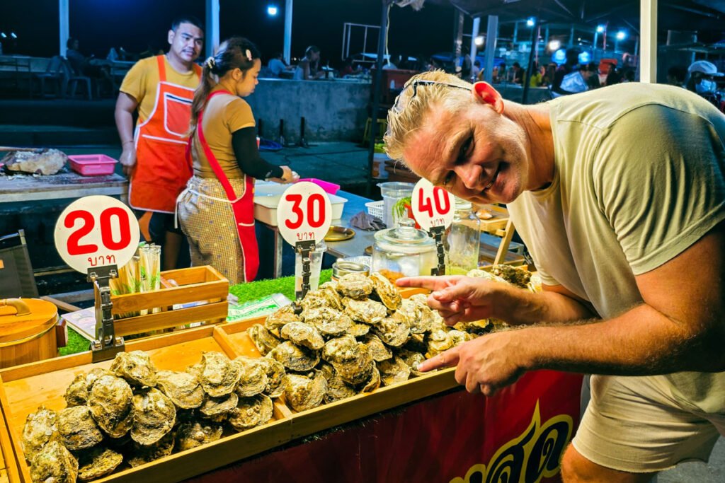 The author is standing at a street food stall pointing at some oysters that are being sold for 20 thb.