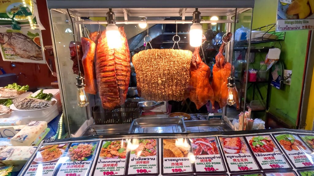 A food stall at the local night market showing some fried dusk, pork skin and ribs. At the bottom prices on various dishes are shown