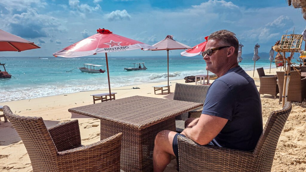 Man sitting on a beach watching the ocean, reflecting on slow travel and settling into a place
