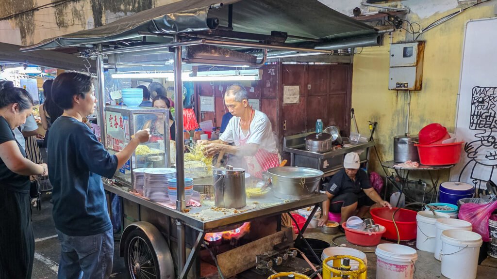 Side view of a street food stand in Asia with a vendor preparing food and people interacting nearby