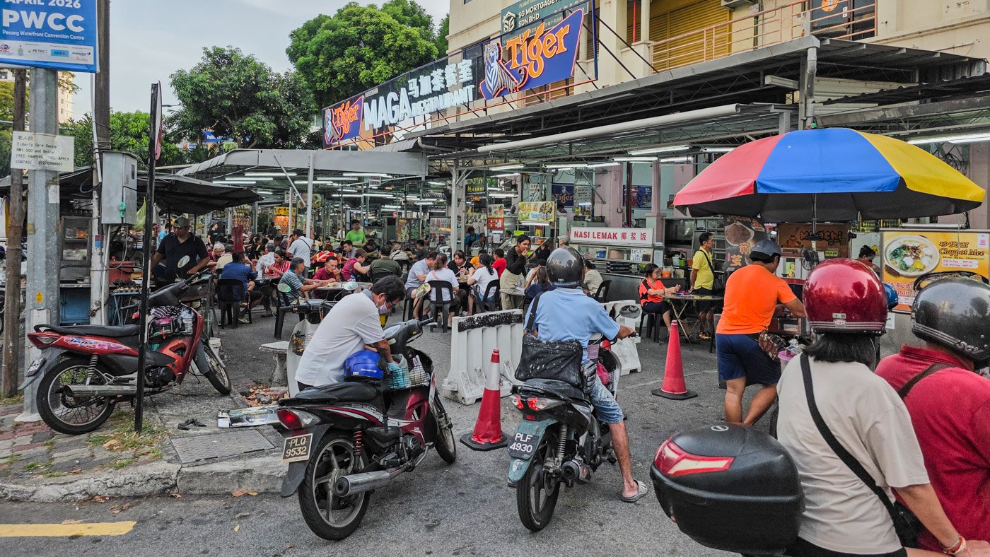 Crowded local food market entrance in Penang with people eating and shopping