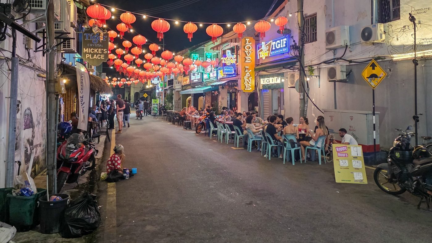 Evening scene on Love Lane in George Town, Penang, showing tourists dining while an elderly woman sits nearby