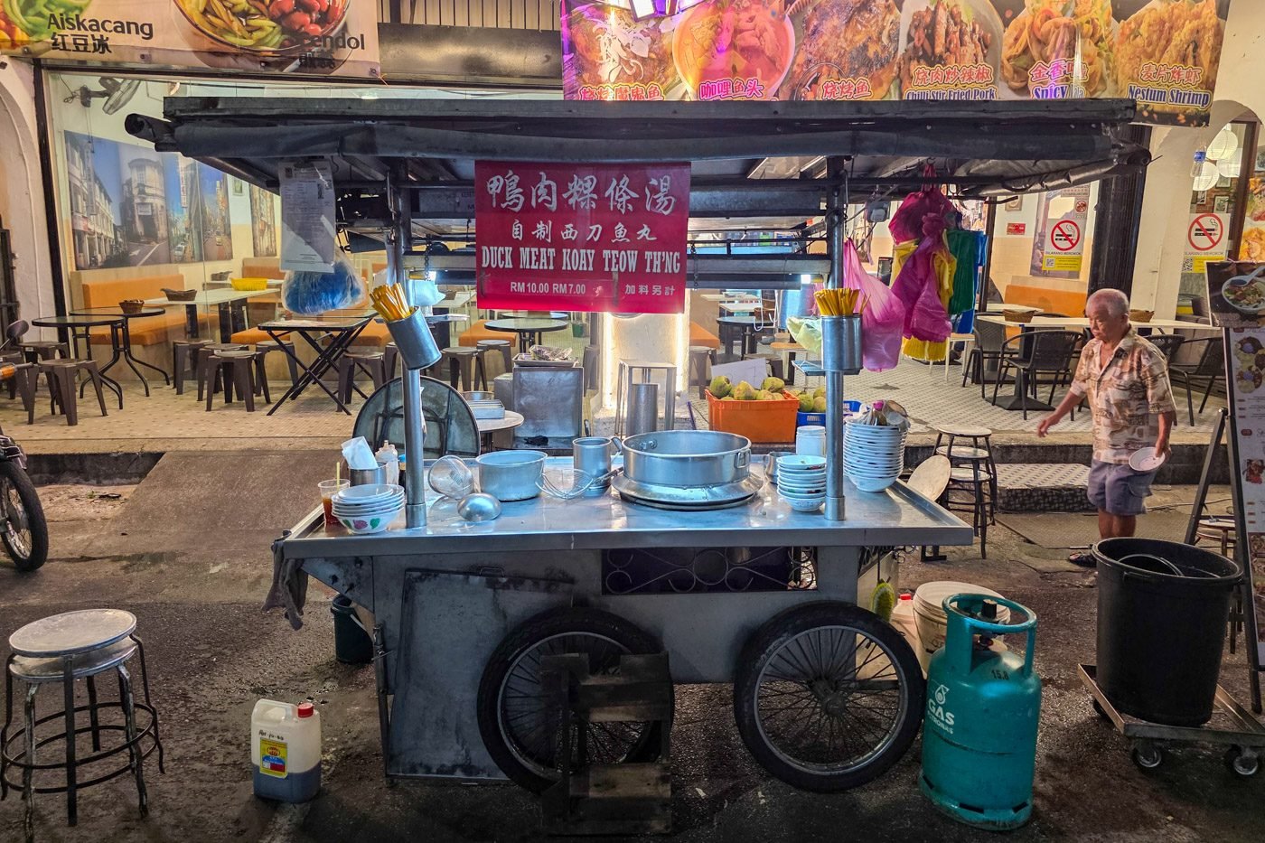 An older man walking past a food stall in George Town, Penang