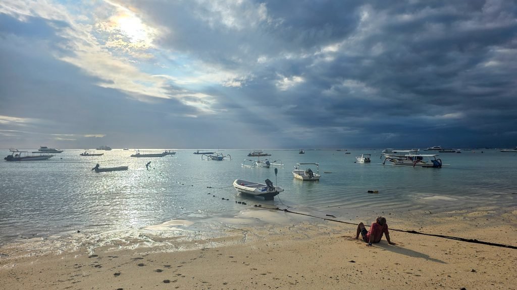 Local man resting on the beach near fishing boats on Nusa Lembongan before rain