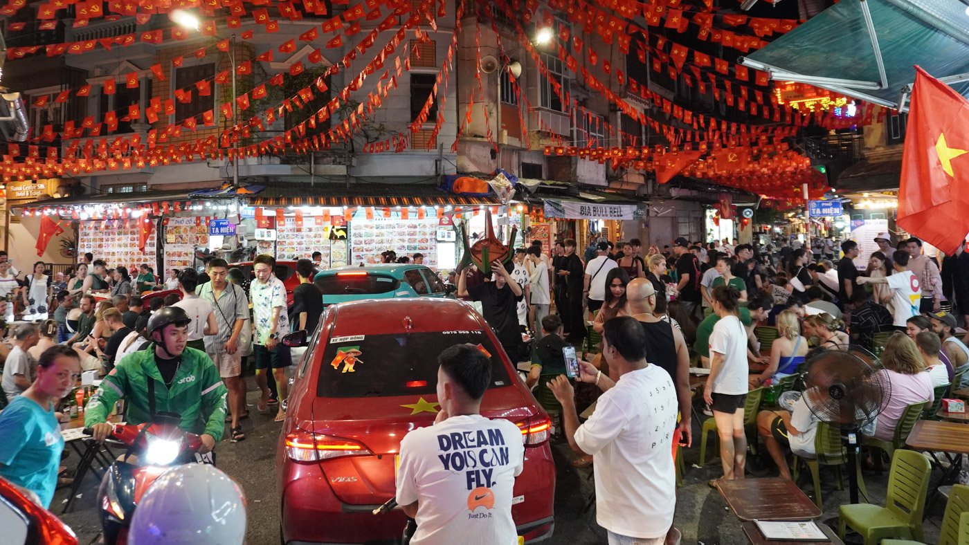 Busy street scene in Hanoi's Old Quarter with restaurants, motorcycles, and pedestrians