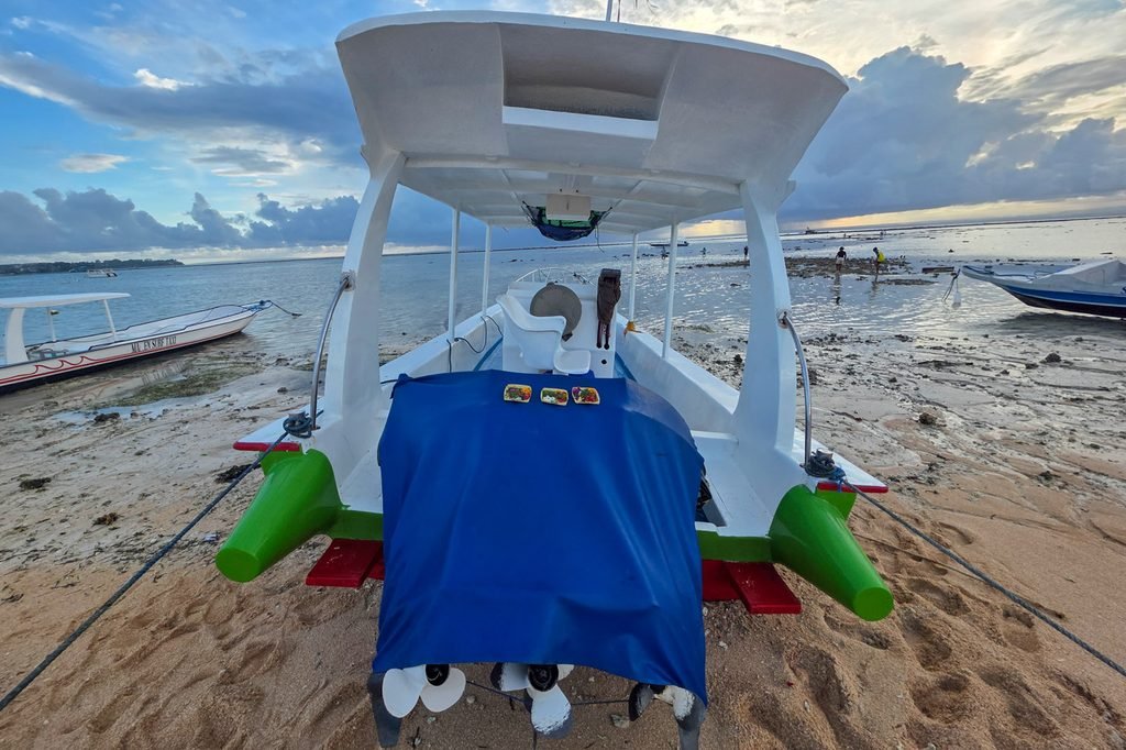Boat resting at low tide with Balinese offerings attached to the motor in Nusa Lembongan