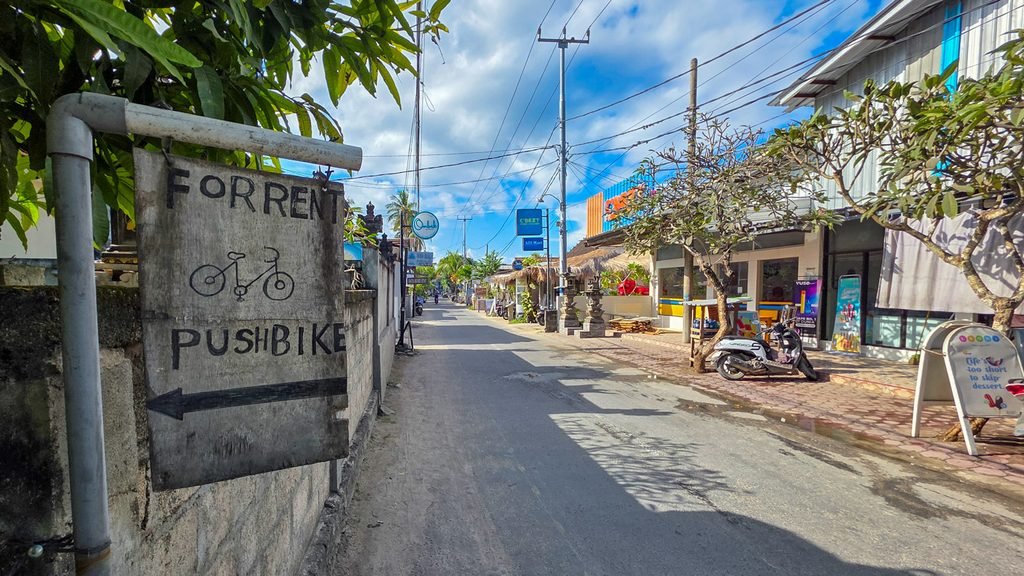 Quiet road in Nusa Lembongan with a parked scooter and bicycle rental sign.