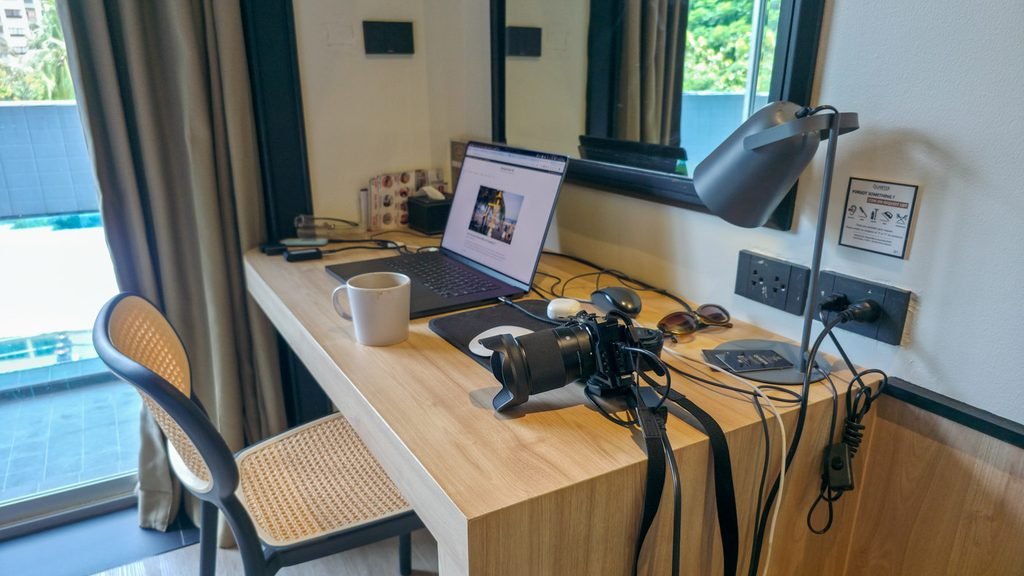 Laptop, coffee, and camera charging on a hotel desk while working as a digital nomad in Bangkok.