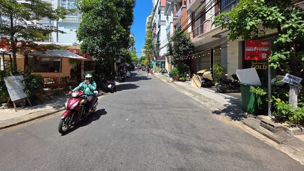 Sunny neighborhood street in Da Nang with cafés, apartments and a scooter