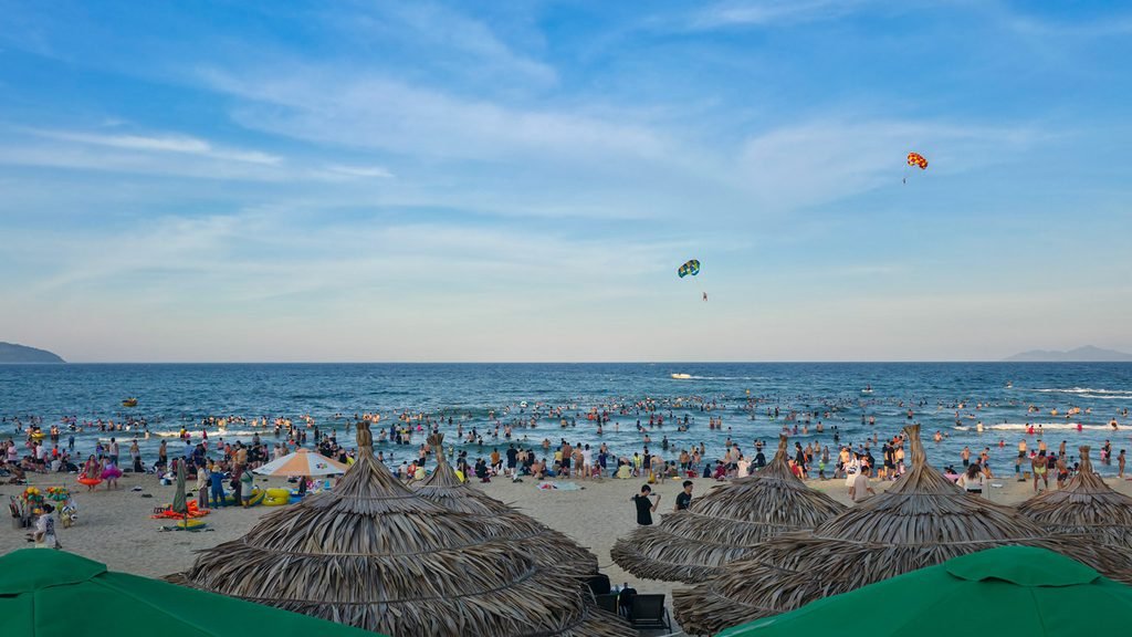 Crowds of people swimming and relaxing along Da Nang's beachfront in the afternoon.