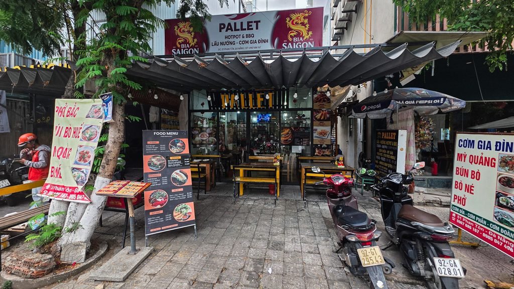 Pallet restaurant in Da Nang, Vietnam, with outdoor tables, Vietnamese food signs, and scooters parked outside.